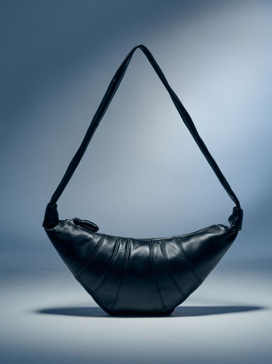 Schwarze Lederhandtasche mit gebogenem Riemen auf blauem Hintergrund.