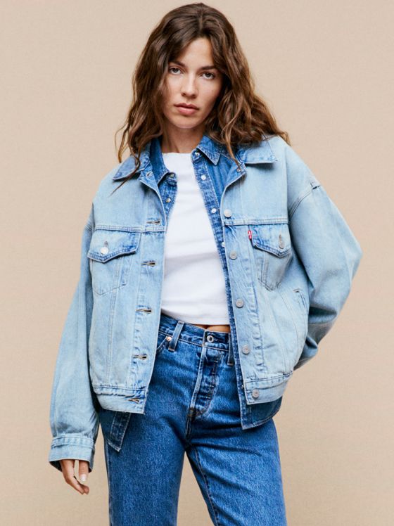 Eine Frau trägt eine hellblaue Jeansjacke über einem weißen T-Shirt und eine passende Jeans.